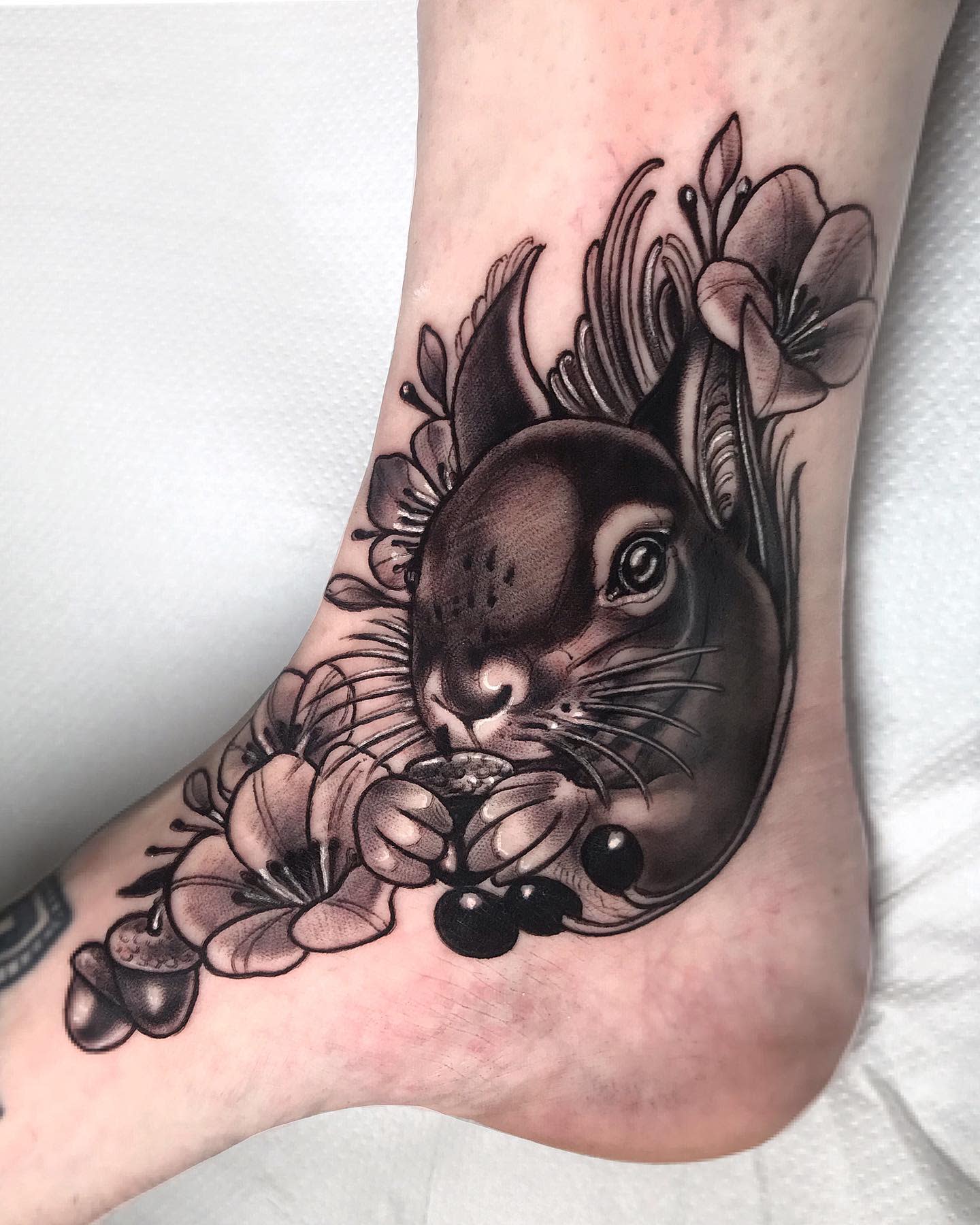 Detailed black and gray squirrel tattoo surrounded by flowers on an ankle
